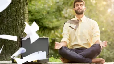 Man meditating outdoors, papers flying from a briefcase